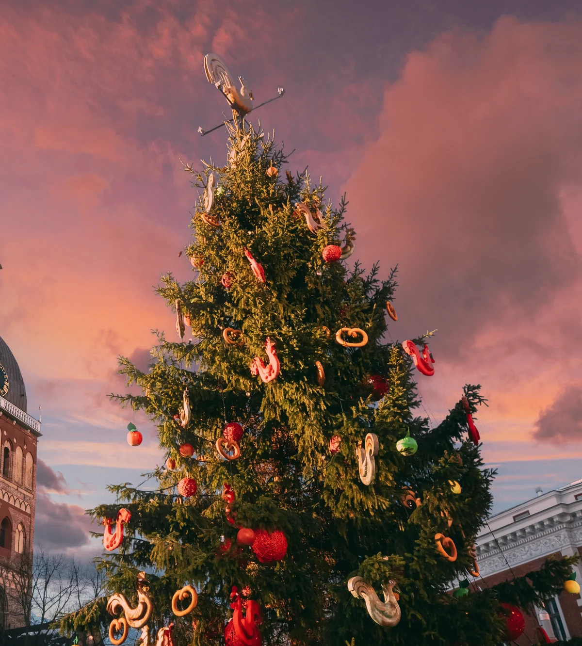 A traditional European Christmas tree decorated with hand-crafted ornaments against a pink and gold sunset sky