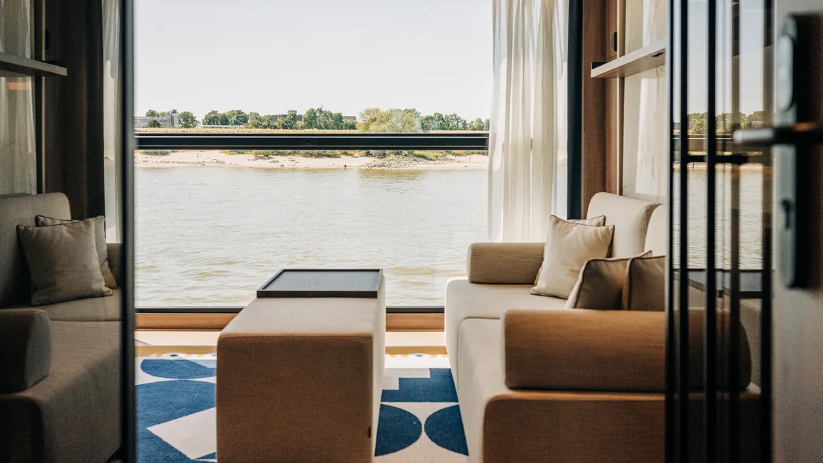Salon de la suite de deux pièces du Transcend Connect, avec canapé et vue pleine hauteur sur la rivière